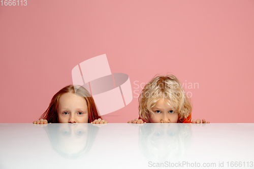 Image of Happy children isolated on coral pink studio background. Look happy, cheerful, sincere. Copyspace. Childhood, education, emotions concept