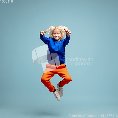 Image of Happy curly boy isolated on blue studio background. Looks happy, cheerful, sincere. Copyspace. Childhood, education, emotions concept