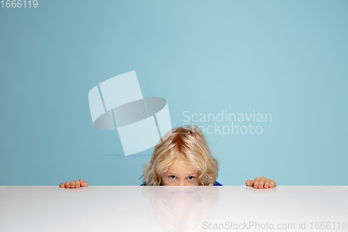 Image of Happy curly boy isolated on blue studio background. Looks happy, cheerful, sincere. Copyspace. Childhood, education, emotions concept