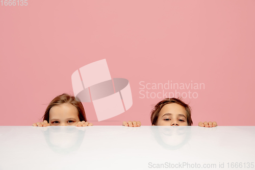 Image of Happy children isolated on coral pink studio background. Look happy, cheerful, sincere. Copyspace. Childhood, education, emotions concept