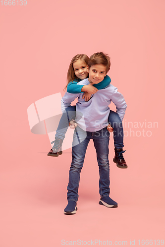 Image of Happy children isolated on coral pink studio background. Look happy, cheerful, sincere. Copyspace. Childhood, education, emotions concept