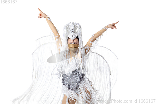 Image of Beautiful young woman in carnival, stylish masquerade costume with feathers dancing on white studio background. Concept of holidays celebration, festive time, fashion