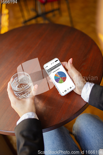 Image of Close up hands holding smartphone with trading information graphs on the screen. Business, finance. Modern tech and work.