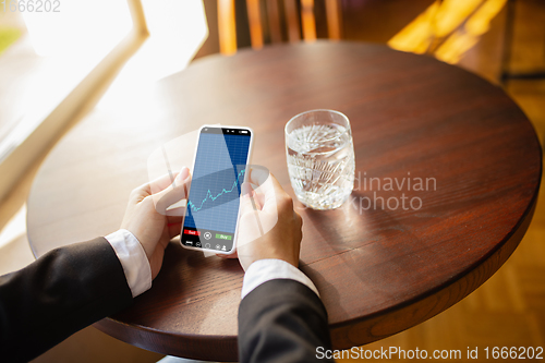 Image of Close up hands holding smartphone with trading information graphs on the screen. Business, finance. Modern tech and work.