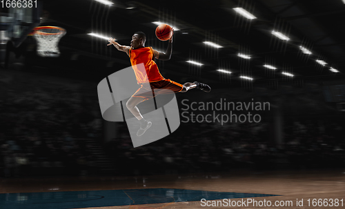 Image of African-american young basketball player in action and flashlights over gym background. Concept of sport, movement, energy and dynamic, healthy lifestyle.