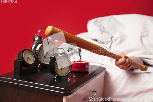 Image of Man wakes up and he\'s mad at clock ringing, switches it off with baseball bat