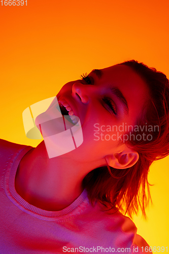 Image of Caucasian woman\'s portrait isolated on orange studio background in multicolored neon light