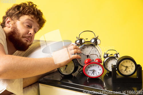 Image of Man wakes up and he\'s mad at clock ringing, trying to switch it off, looks sleepy