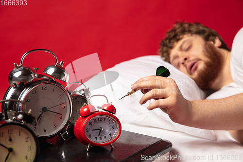 Image of Man wakes up and he\'s mad at clock ringing, switches it off with dart