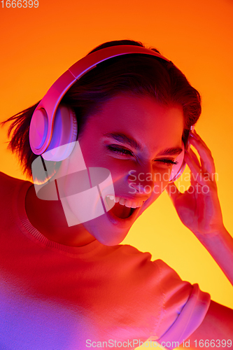 Image of Caucasian woman\'s portrait isolated on orange studio background in multicolored neon light