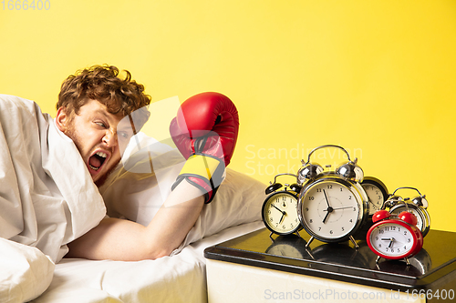 Image of Man wakes up and he\'s mad at clock ringing, switches it off with the boxing glove