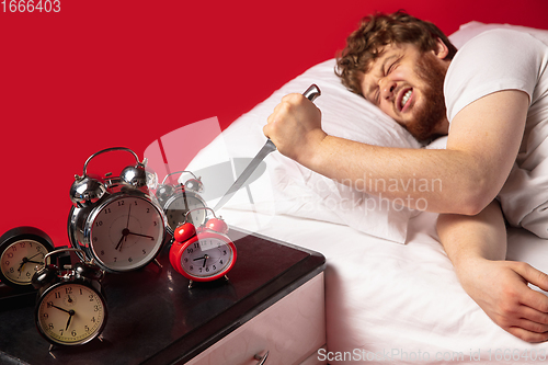 Image of Man wakes up and he\'s mad at clock ringing, switches it off with kitchen knife