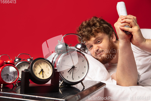 Image of Man wakes up and he\'s mad at clock ringing, switches it off with rolled documents