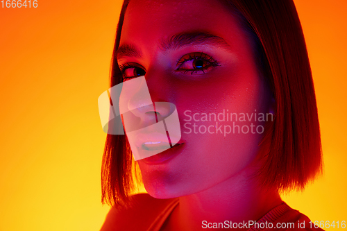 Image of Caucasian woman\'s portrait isolated on orange studio background in multicolored neon light