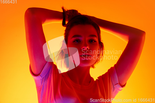 Image of Caucasian woman\'s portrait isolated on orange studio background in multicolored neon light