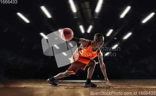 Image of African-american young basketball player in action and flashlights over gym background. Concept of sport, movement, energy and dynamic, healthy lifestyle.