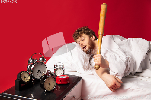 Image of Man wakes up and he\'s mad at clock ringing, switches it off with baseball bat