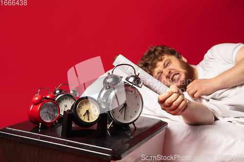 Image of Man wakes up and he\'s mad at clock ringing, switches it off with rolled documents