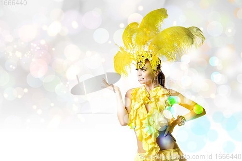 Image of Beautiful young woman in carnival, stylish masquerade costume with feathers dancing on white studio background with shining bokeh