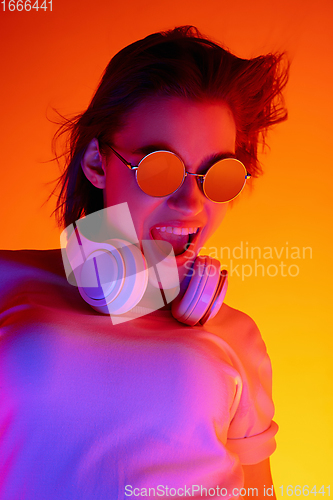 Image of Caucasian woman\'s portrait isolated on orange studio background in multicolored neon light
