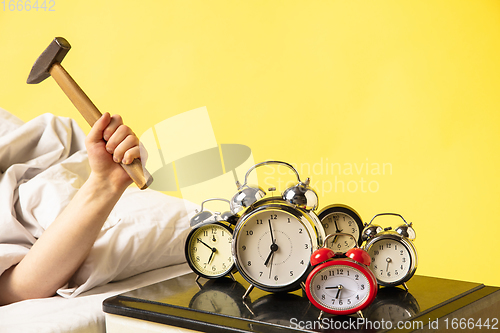 Image of Man wakes up and he\'s mad at clock ringing, switches it off with the hammer