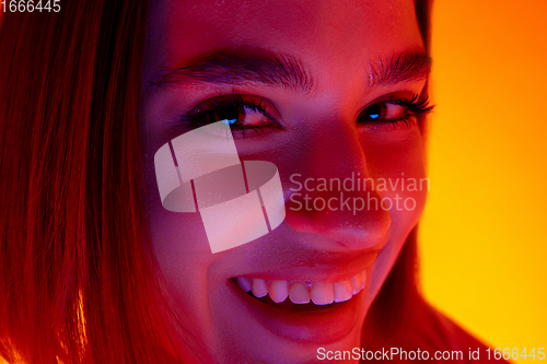 Image of Caucasian woman\'s portrait isolated on orange studio background in multicolored neon light