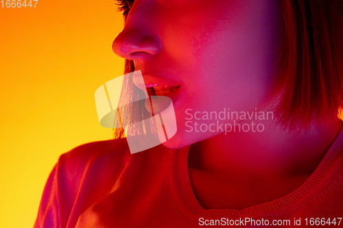 Image of Caucasian woman\'s portrait isolated on orange studio background in multicolored neon light