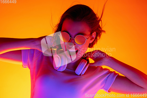 Image of Caucasian woman\'s portrait isolated on orange studio background in multicolored neon light