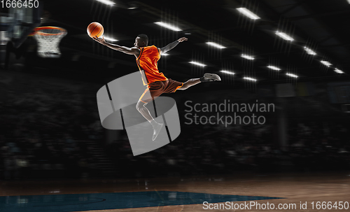 Image of African-american young basketball player in action and flashlights over gym background. Concept of sport, movement, energy and dynamic, healthy lifestyle.