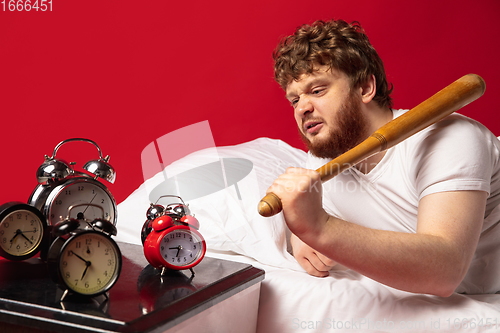 Image of Man wakes up and he\'s mad at clock ringing, switches it off with baseball bat