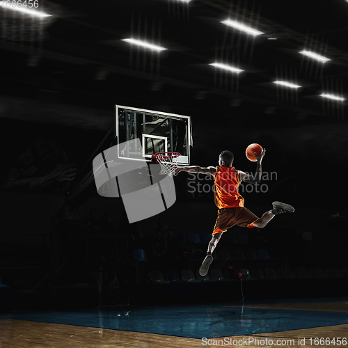 Image of African-american young basketball player in action and flashlights over gym background. Concept of sport, movement, energy and dynamic, healthy lifestyle.