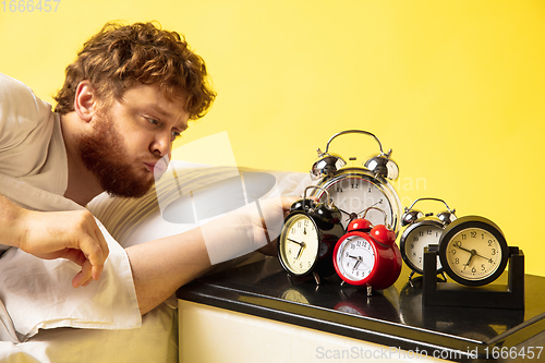 Image of Man wakes up and he\'s mad at clock ringing, trying to switch it off, looks sleepy