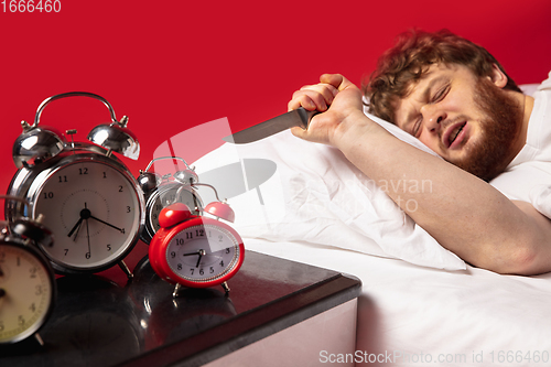 Image of Man wakes up and he\'s mad at clock ringing, switches it off with kitchen knife