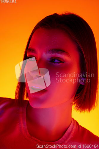 Image of Caucasian woman\'s portrait isolated on orange studio background in multicolored neon light