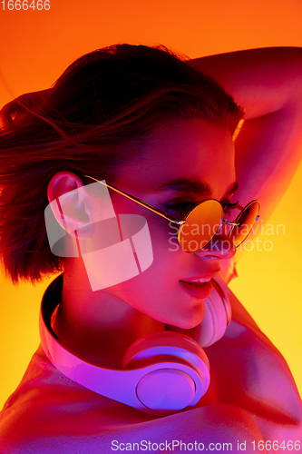 Image of Caucasian woman\'s portrait isolated on orange studio background in multicolored neon light