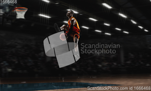 Image of African-american young basketball player in action and flashlights over gym background. Concept of sport, movement, energy and dynamic, healthy lifestyle.