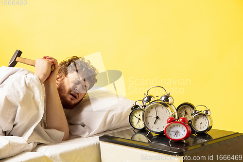 Image of Man wakes up and he\'s mad at clock ringing, switches it off with the hammer