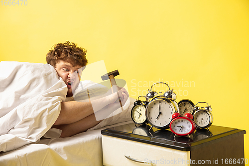 Image of Man wakes up and he\'s mad at clock ringing, switches it off with the hammer