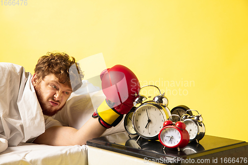 Image of Man wakes up and he\'s mad at clock ringing, switches it off with the boxing glove