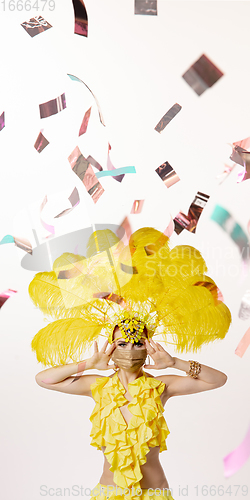 Image of Beautiful young woman in carnival, stylish masquerade costume with feathers dancing on white studio background with shining confetti