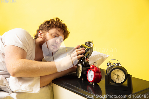 Image of Man wakes up and he\'s mad at clock ringing, trying to switch it off, looks sleepy