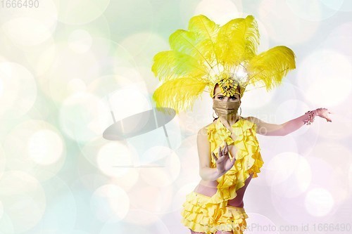 Image of Beautiful young woman in carnival, stylish masquerade costume with feathers dancing on white studio background with shining bokeh