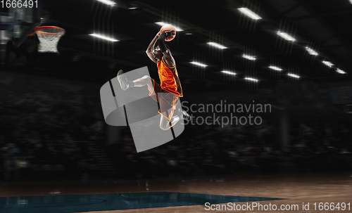 Image of African-american young basketball player in action and flashlights over gym background. Concept of sport, movement, energy and dynamic, healthy lifestyle.