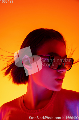 Image of Caucasian woman\'s portrait isolated on orange studio background in multicolored neon light