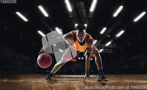 Image of African-american young basketball player in action and flashlights over gym background. Concept of sport, movement, energy and dynamic, healthy lifestyle.