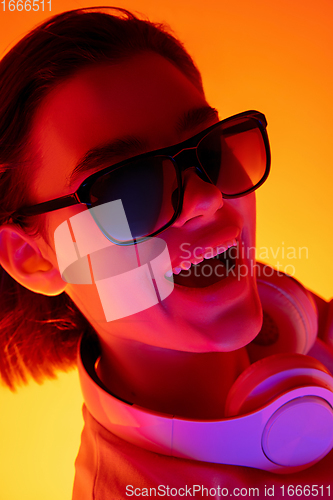 Image of Caucasian woman\'s portrait isolated on orange studio background in multicolored neon light