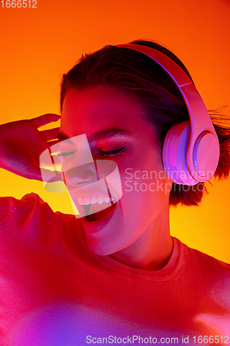 Image of Caucasian woman\'s portrait isolated on orange studio background in multicolored neon light