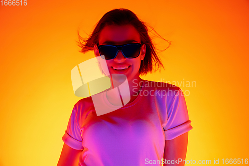 Image of Caucasian woman\'s portrait isolated on orange studio background in multicolored neon light