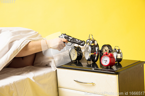 Image of Man wakes up and he\'s mad at clock ringing, switches it off with the gun