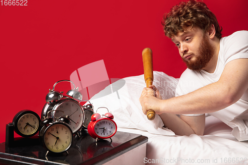 Image of Man wakes up and he\'s mad at clock ringing, switches it off with baseball bat